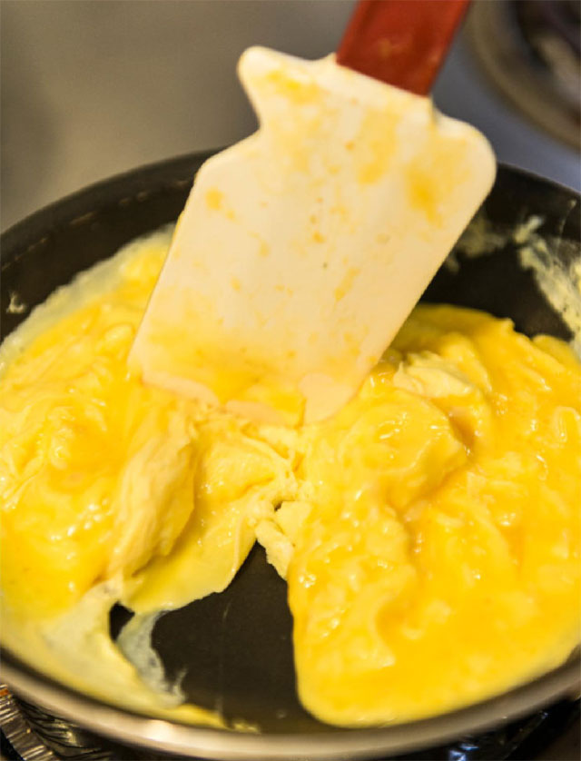 Scramled eggs and a spatula share a frying pan